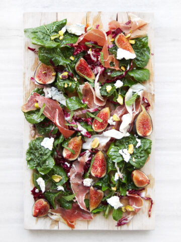fig salad with arugula, prosciutto, and pistachios on wooden board